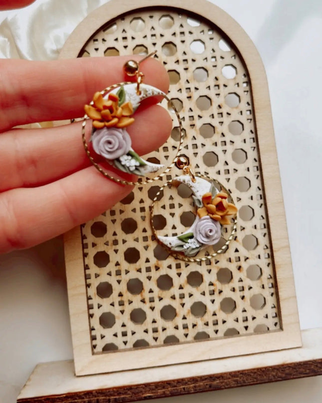 Hand holding a floral earring with a decorative wooden stand in the background