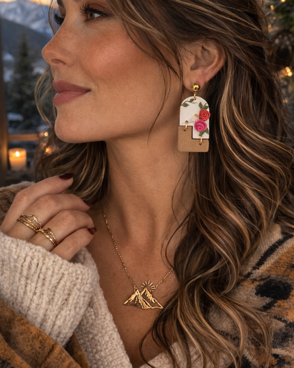 Woman wearing floral earrings with a mountain necklace outdoors